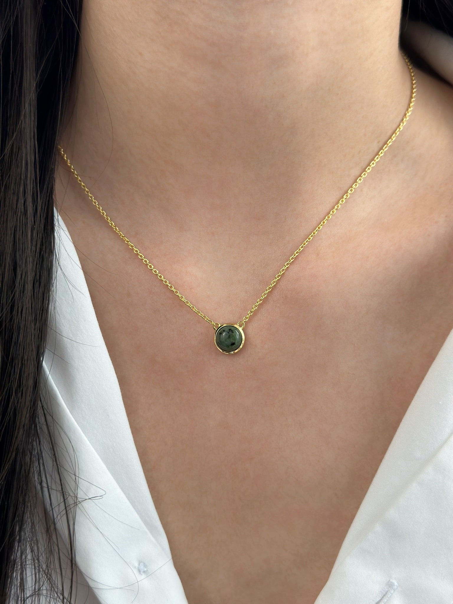 Woman in white dress shirt displays gold jade necklace