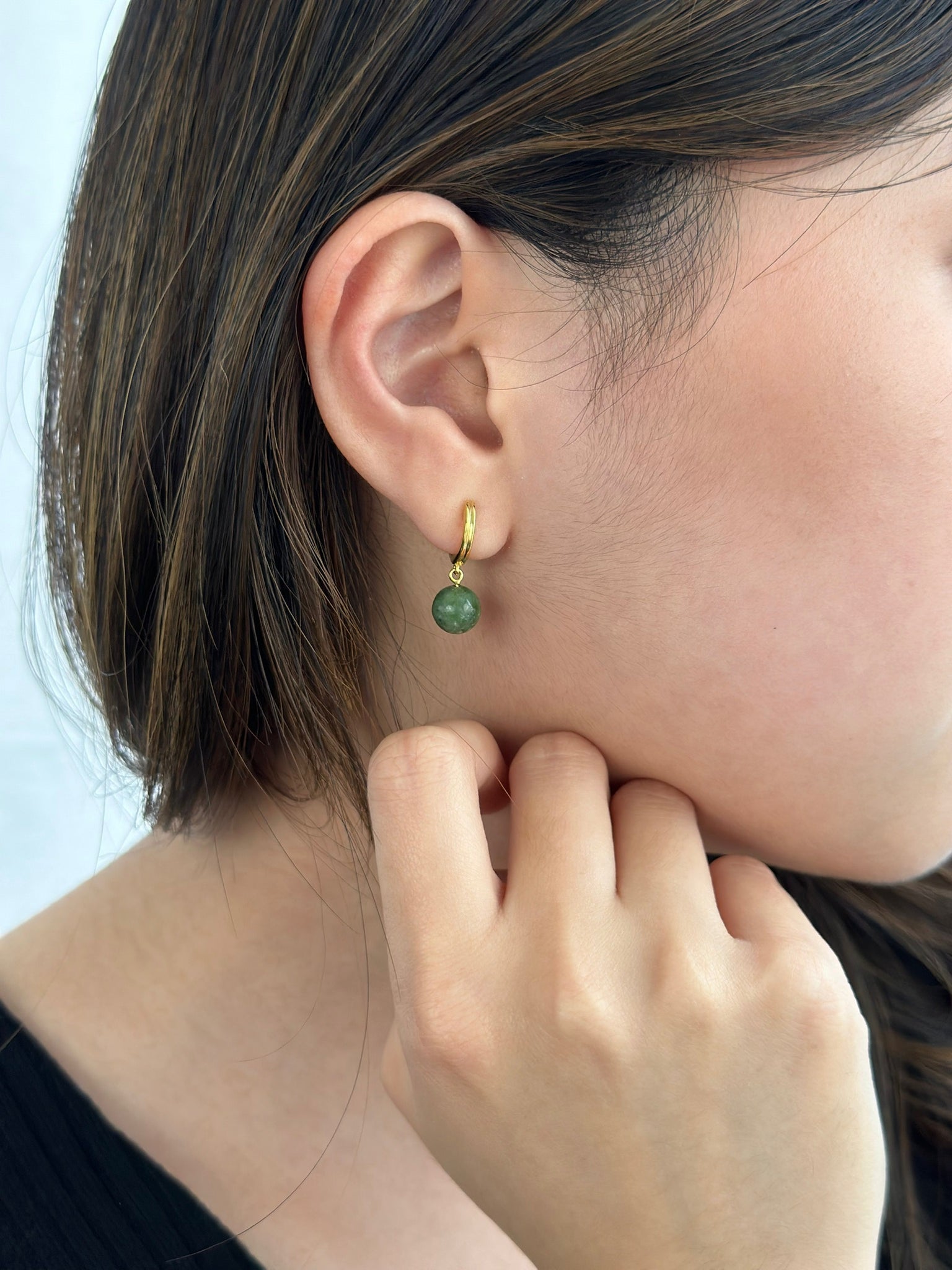 Woman wearing gold jade hoop earring resting on her fist