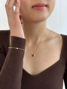 Woman wearing brown dress with hand on cheek displaying gold jade necklace and gold jade and pearl bracelet