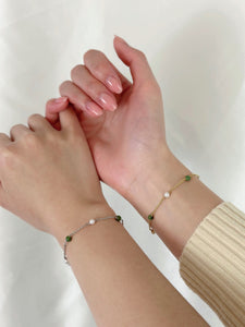 Two hands intertwined wearing gold and silver jade and pearl bracelets