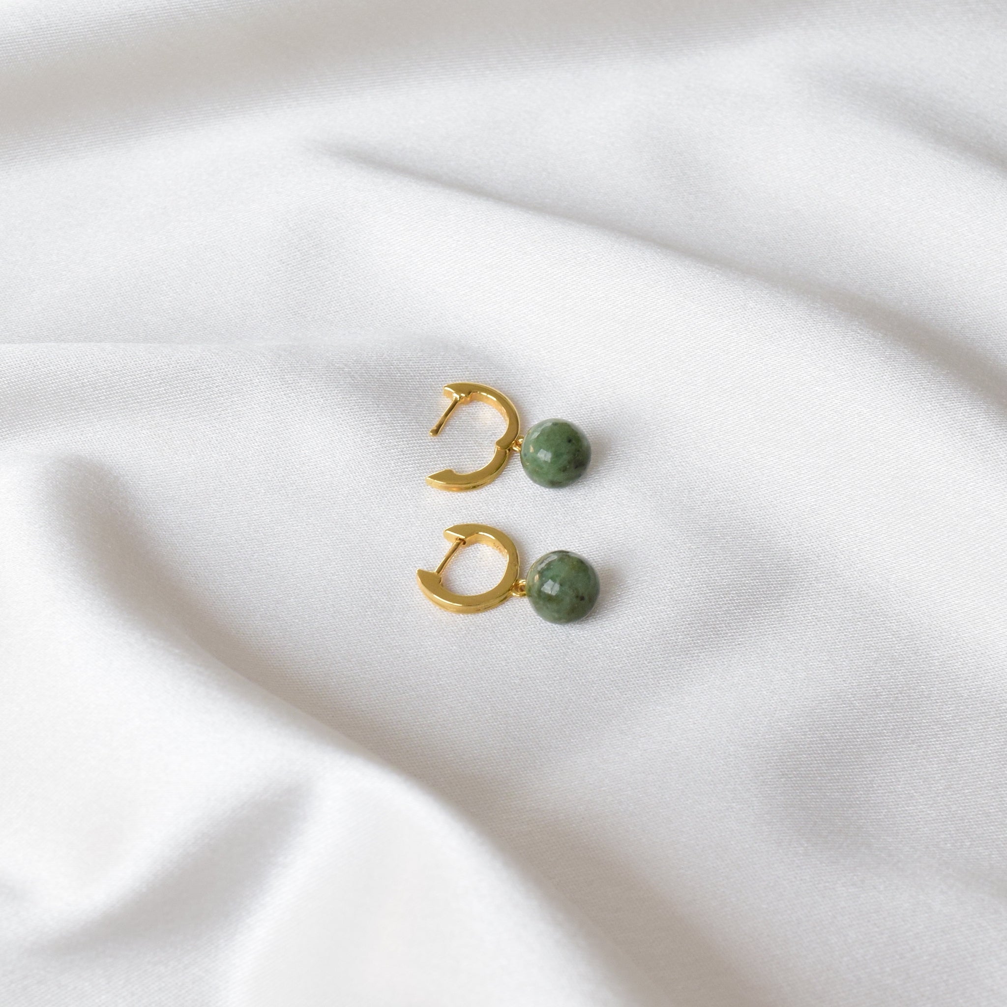 Gold jade hoop earrings displayed on cloth