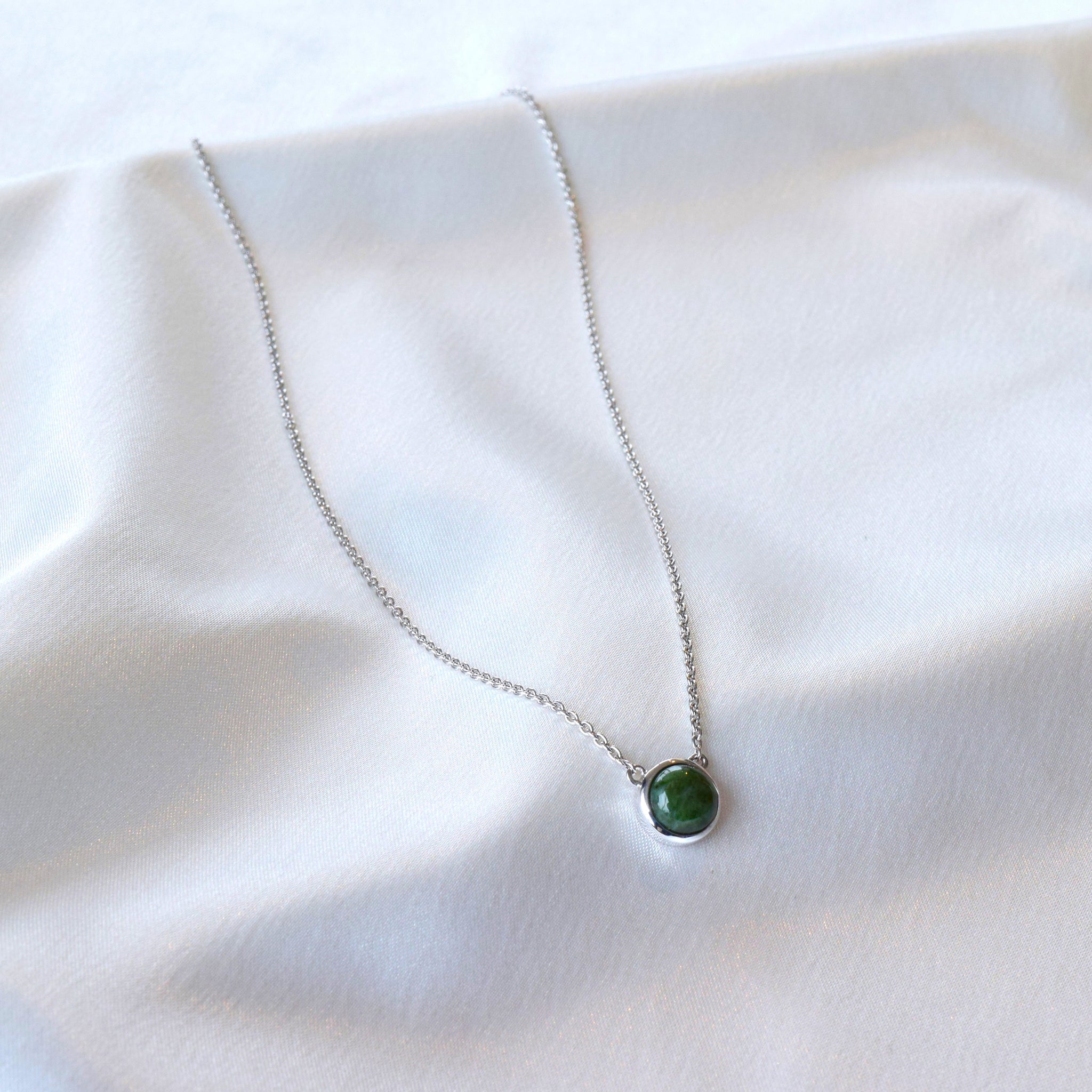 Silver jade necklace hanging on cloth