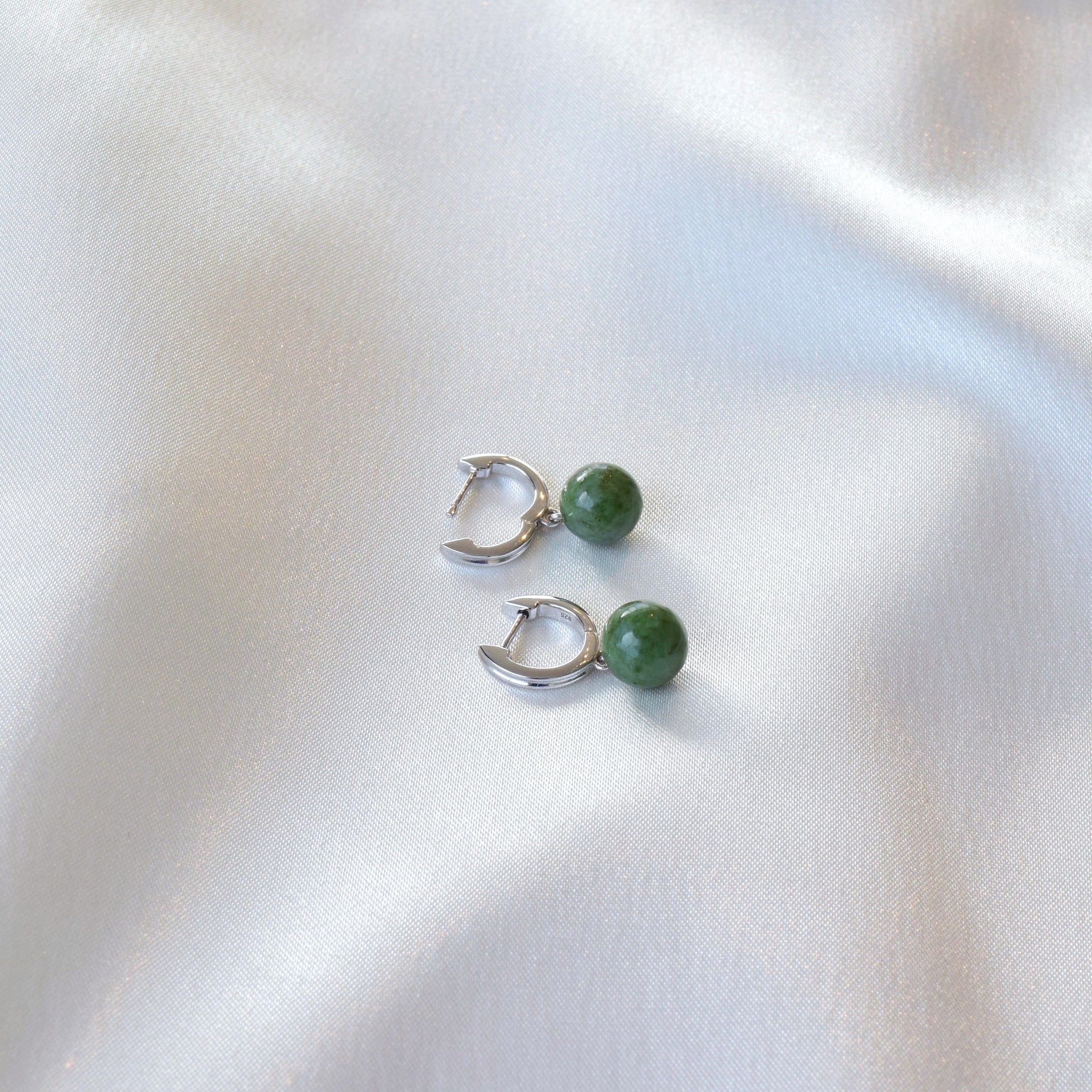 Closeup of silver jade hoop earrings laying on cloth