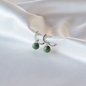 Closeup of silver jade earrings hanging on cloth