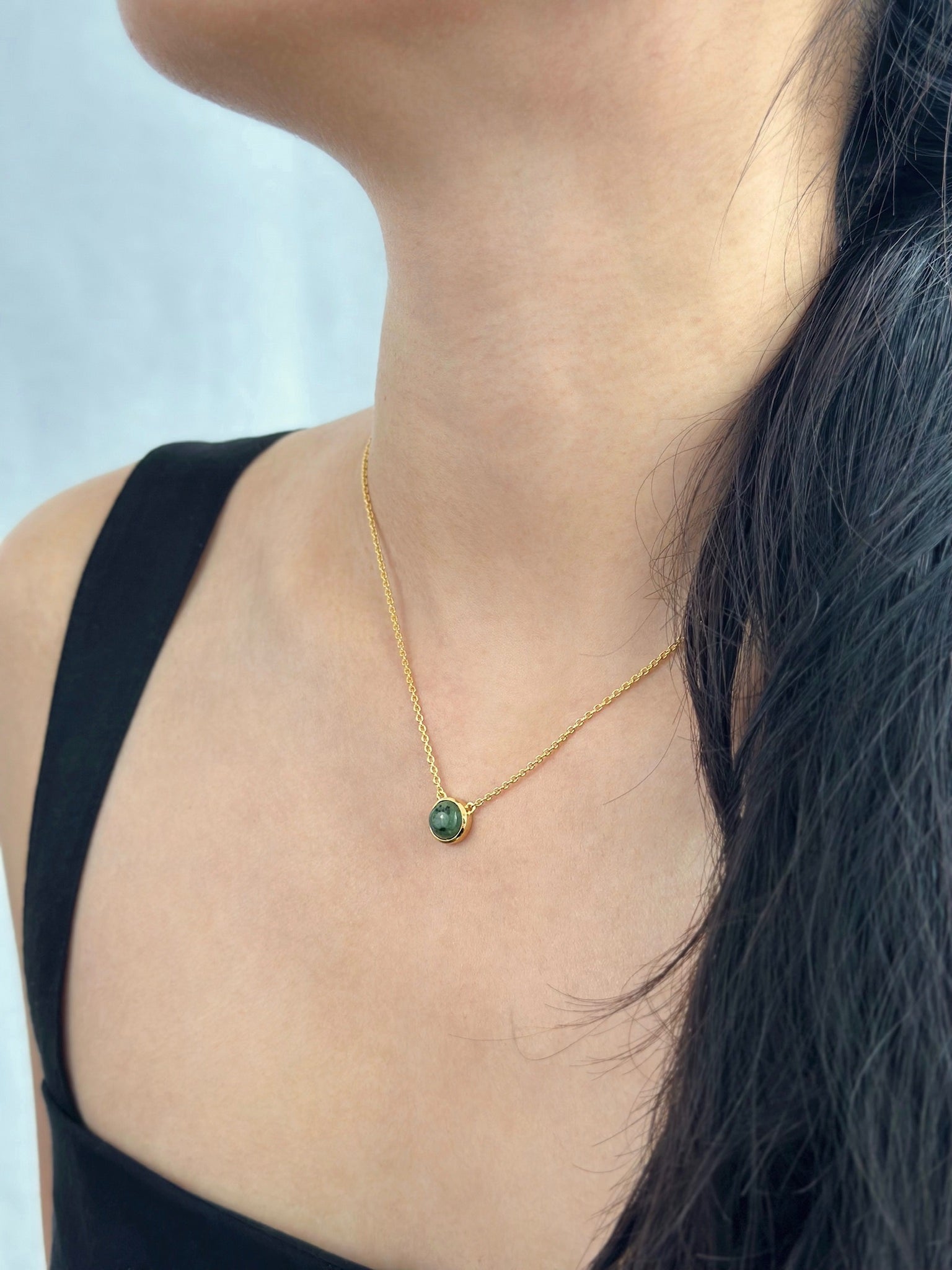 Woman wearing black dress displays gold jade necklace