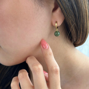 Woman with pink nails pointing at gold jade hoop earrings 