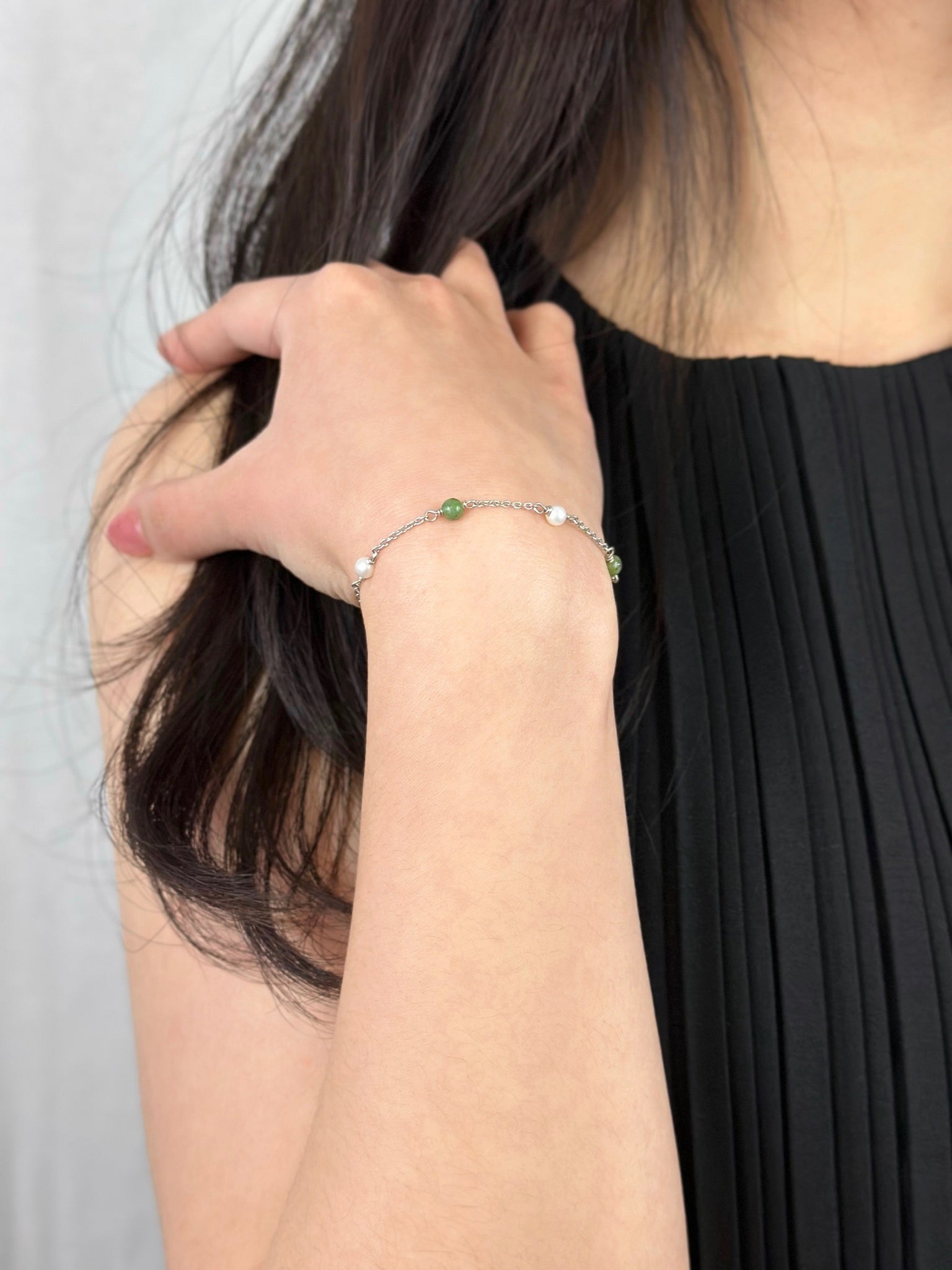 Woman with hand on shoulder displaying silver hade and pearl bracelet