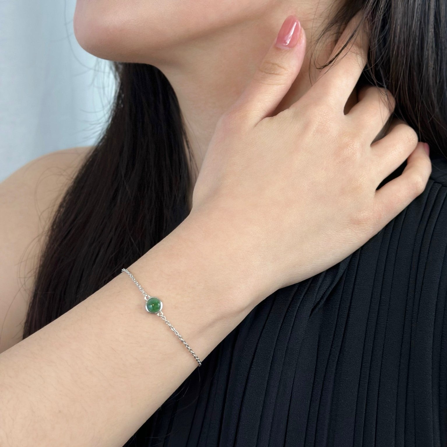 Woman wearing black dress with her hand on her neck displaying silver jade bracelet