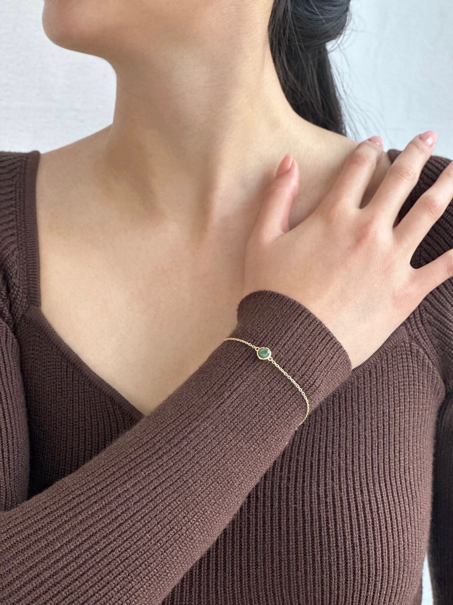 Woman in brown dress displaying gold jade bracelet on her wrist