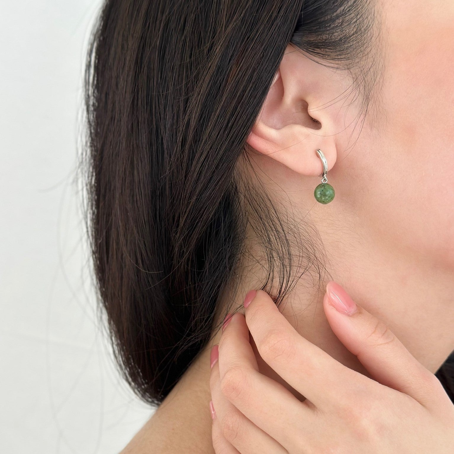 Woman with hand on her neck displaying silver jade hoop earrings