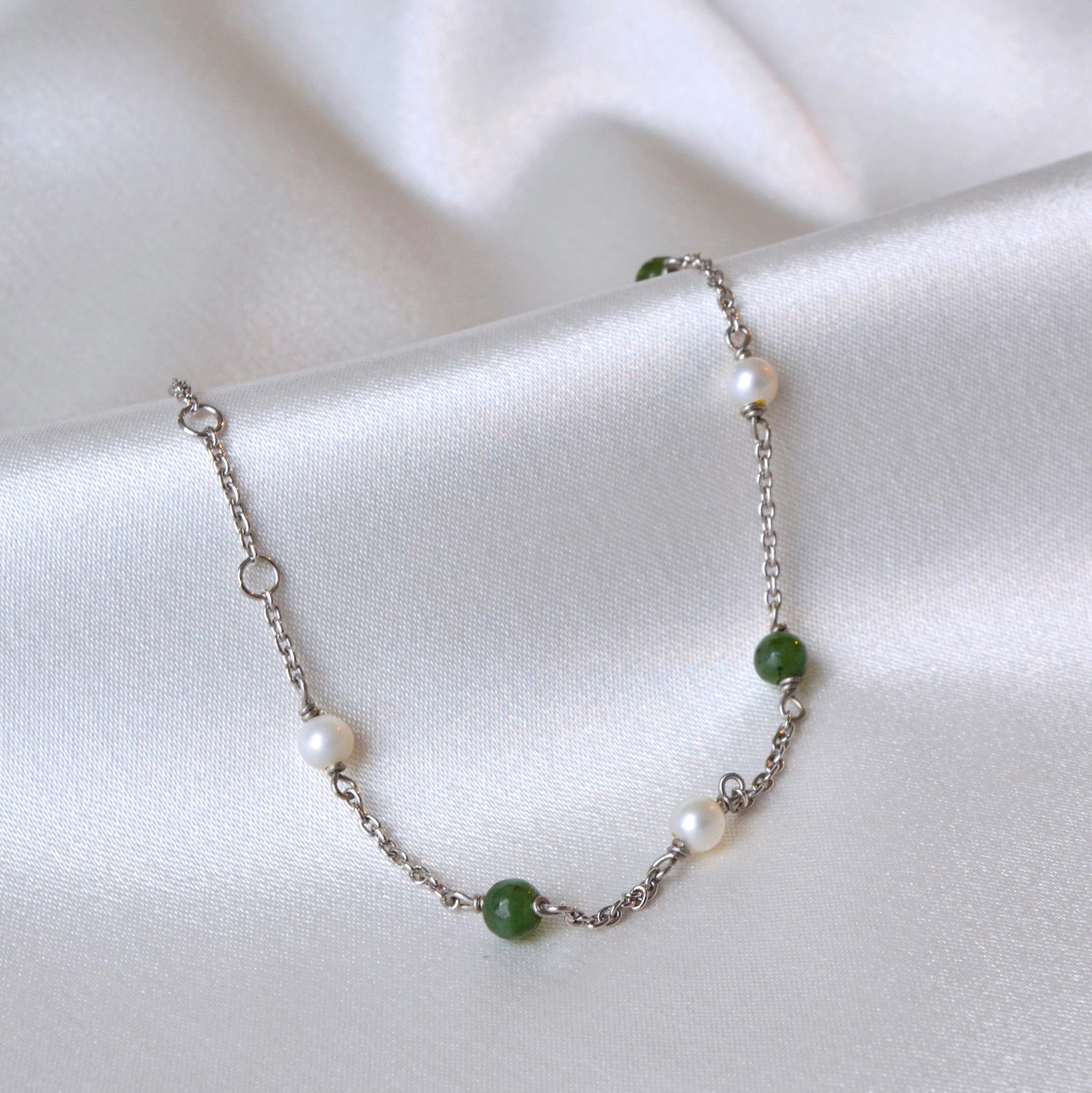 Silver jade and pearl bracelet displayed hanging in a U shape on cloth